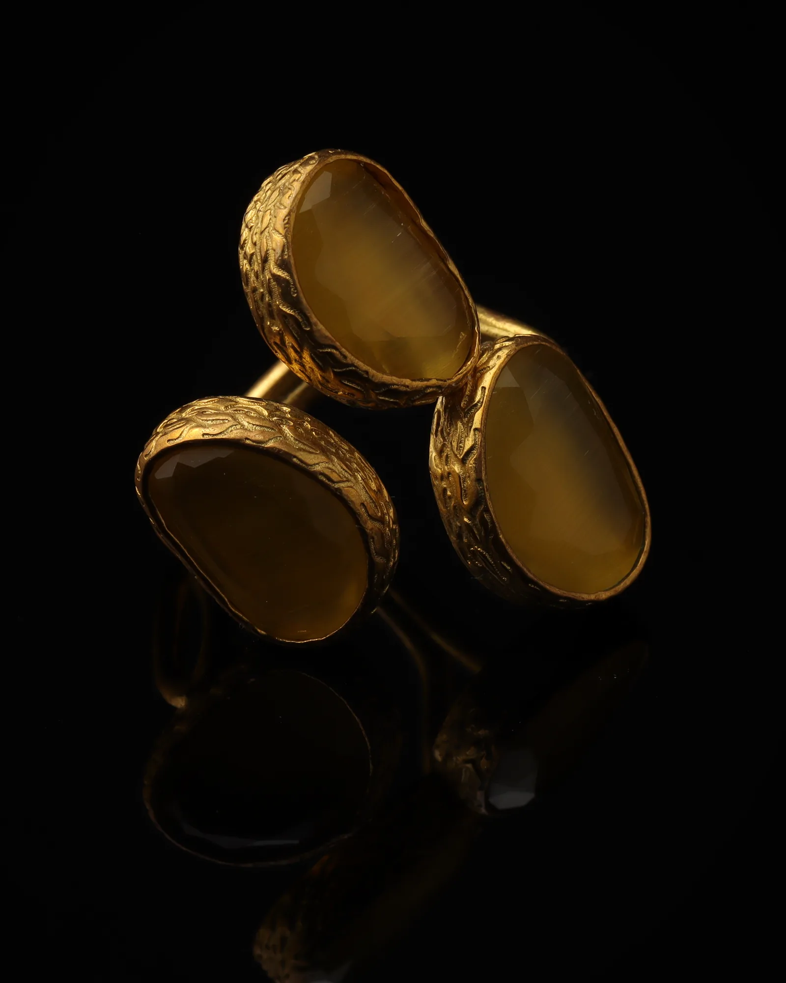Saffron & Walnut - a gold-plated ring with three yellow and brown cat eye stones, on black