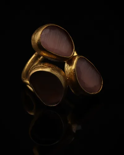 Heather & Mulberry - a gold-plated ring with three pink and plum cat eye stones, on black