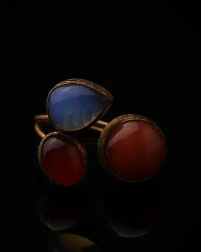 Cornflower & Vermillion - a gold-plated ring with three blue and red cat eye stones, on black