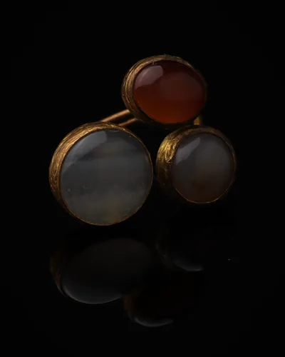 Cinnamon & Dove - a gold-plated ring with three red and grey cat eye stones, on black